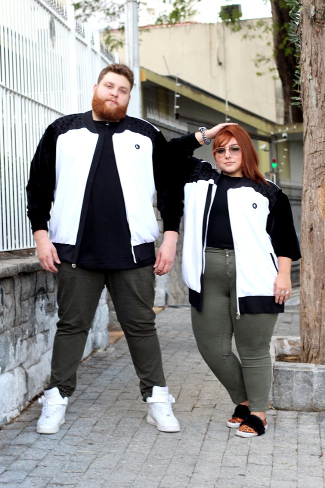 look casal ju romano Casal posando na rua com blusa de frio preto e branca igual, camiseta preta igual, e calça verde militar igual. Os dois estão com aparência séria.