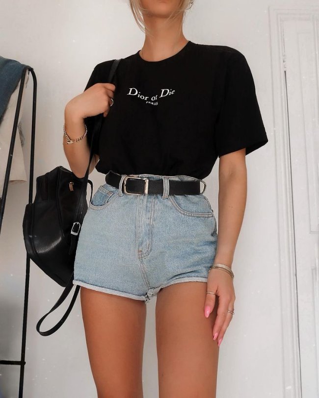 Foto do look de uma mulher. Ela usa camiseta preta, short jeans com cinto preto e mochila preta.