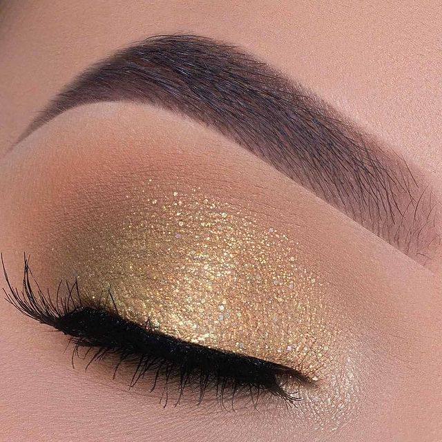 maquiagem com glitter dourado Foto com foco em um olho fechado exibindo a sombra dourada.