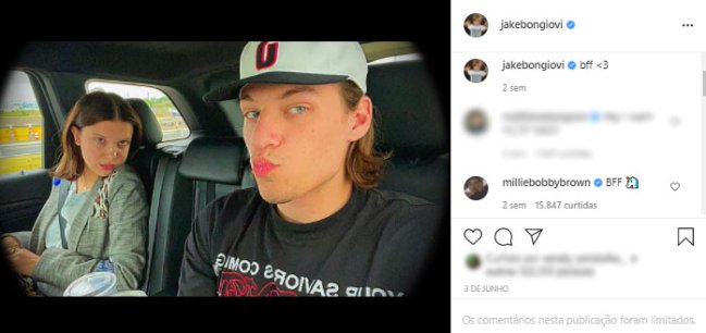 millie-bobby-brown-jake-bongiovi-selfie-carro Millie Bobby Brown sentada no banco do passageiro de um carro, olha para a câmera com o queixo sobre o ombro. No banco do passageiro, Jake, usando boné, faz bico para a câmera