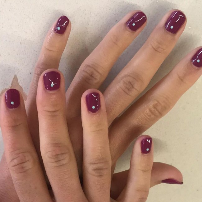 Foto com destaque nas unhas com nail art de bolinha, dessa vez com fundo roxo e bolinha branca.