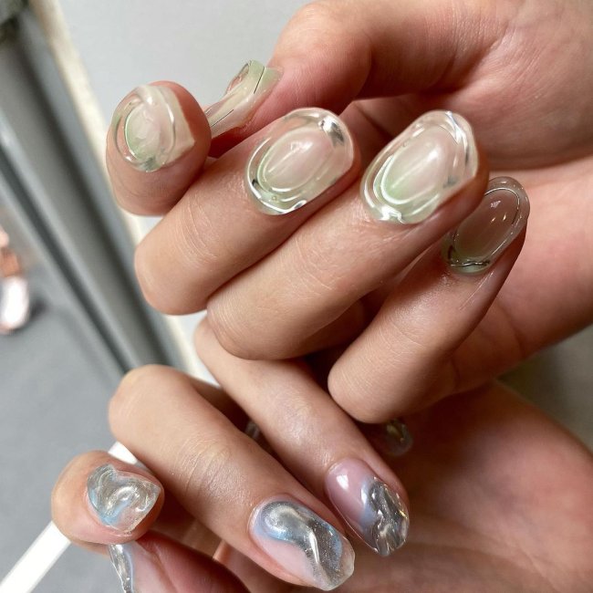 nail art com jelly cinza Foto com foco nas unhas com gel e cinza. Na foto conseguimos ver duas mãos com dedos dobrados.
