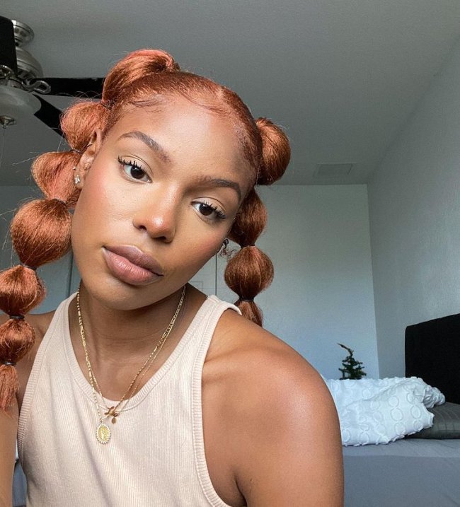 penteado bolha Selfie de uma mulher com maria chiquinha com penteado bolha. Ela usa uma regata bege, colar dourado e está com uma maquiagem leve. Ela olha para a câmera e não sorri.
