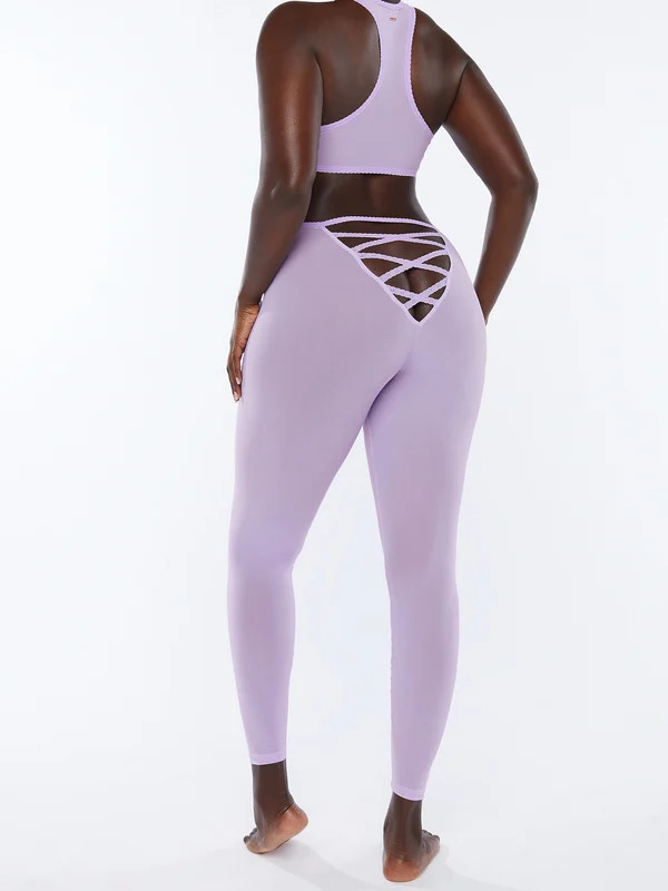 rihanna-legging-savage-x-fenty-bumbum Modelo está de costas vestindo um top e uma calça legging esportiva na cor lilás. A calça possui um recorte em tiras no bumbum, deixando uma parte dele à mostra.