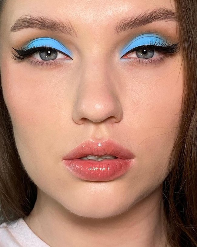 sombra colorida Jovem com expressão séria, a imagem foca em seu rosto com sombra azul e lábios com liptint.
