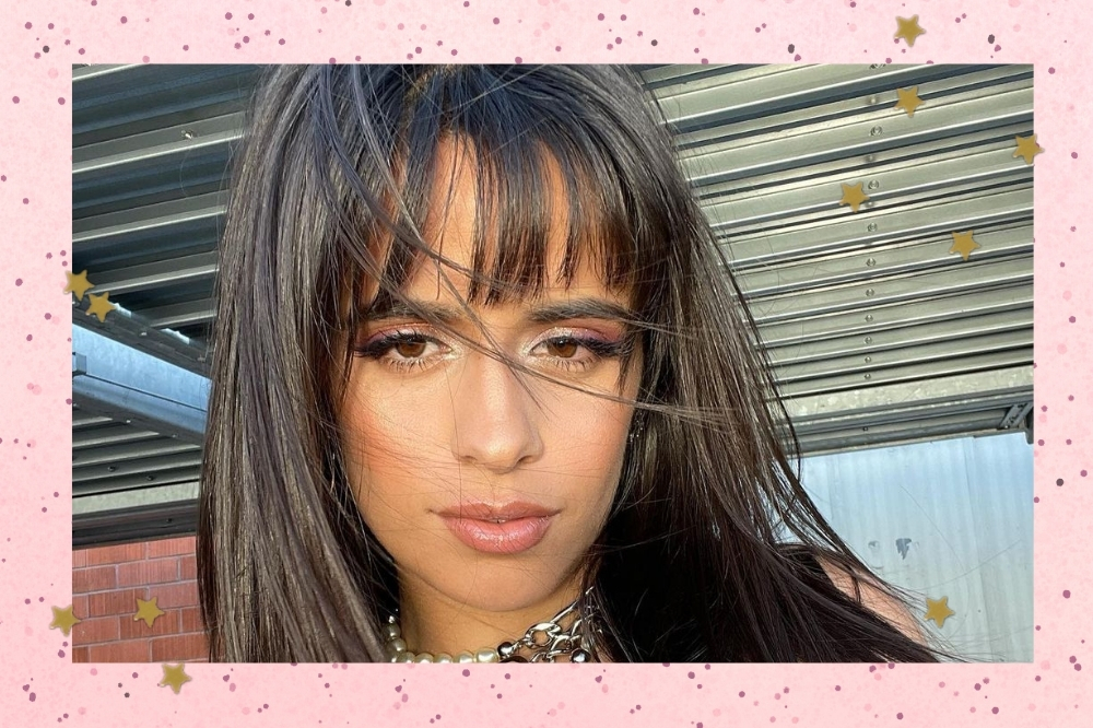 Camila Cabello tirando selfie maquiada e com uma mecha do seu cabelo em seu rosto por conta do vento. Ela usa franjinha e colares.