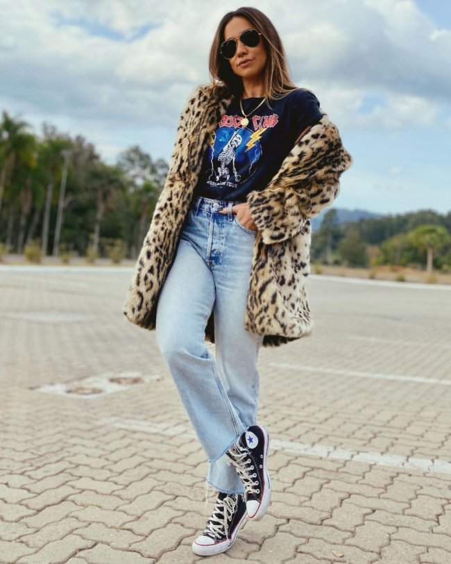 allstar e camiseta de banda Jovem posando no estacionamento usando calça jeans, camiseta de banda, all star e casaco com estampa animal print.