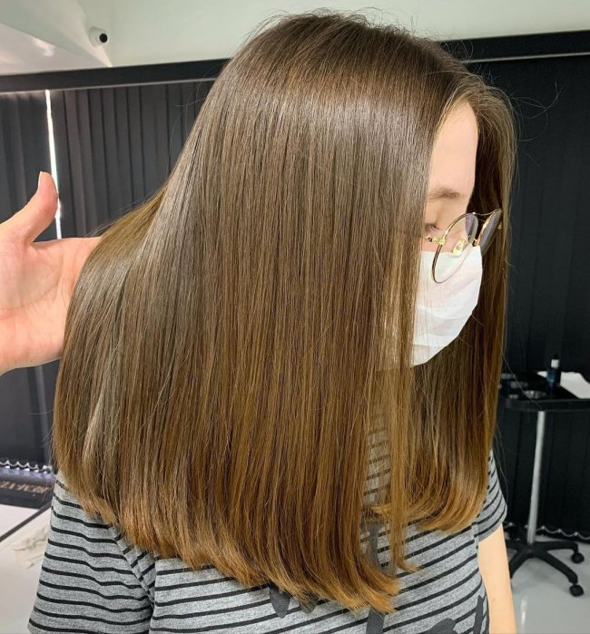 Jovem com a cabeça abaixada, usando blusa listrada, alguém está levantando uma parte de seu cabelo.