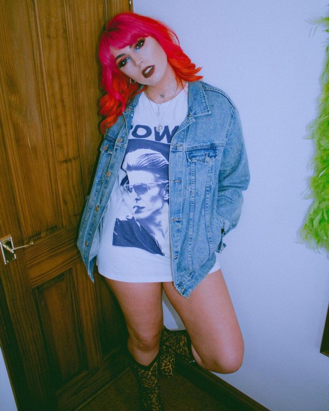 camiseta como vestido Jovem com camiseta branca de banda, jaqueta jeans e posando com as mãos no bolso.