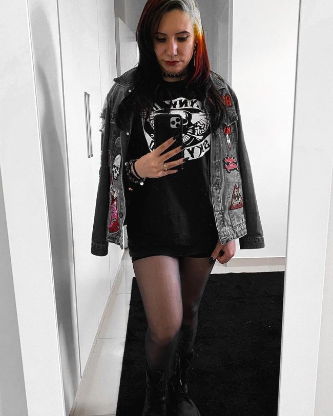camiseta de banda com jaqueta jeans Jovem posando em corredor branco, tirando foto de frente a espelho com jaqueta jeans e blusa de banda sendo usada como vestido.