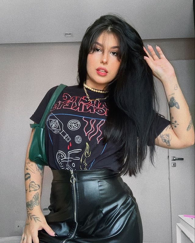 camiseta de banda com saia de couro Jovem posando com a mão direita apoiada na cabeça, usando camiseta de banda e saia de couro preta.