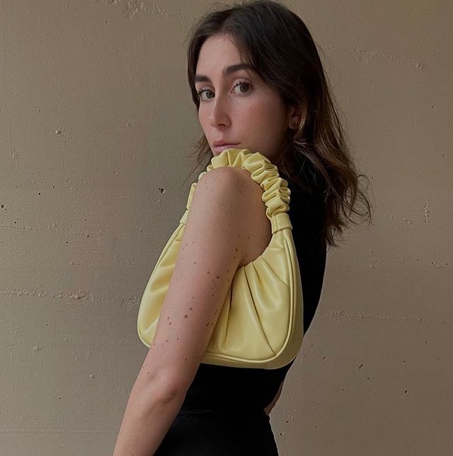 influenciadora com a bolsa jw pei gabbi Jovem posando de lado com a bolsa amarela no ombro, ela usa blusa preta e sua expressão é séria.