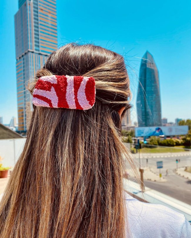 Na imagem só podemos ver alguém de costa, com o cabelo preso com uma presilha rosa com detalhes em vermelho.