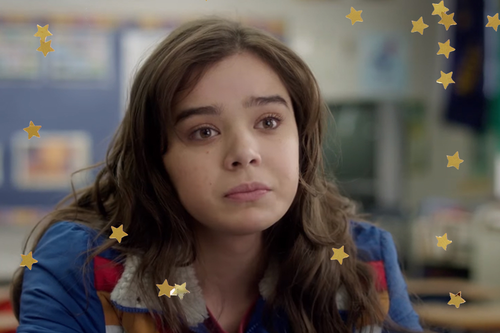 Hailee Steinfeld em cena do filme Quase 18; ela está olhando para frente com uma expressão triste e usa um casaco azul com detalhes amarelos e vermelhos; estrelas amarelas decoram a imagem