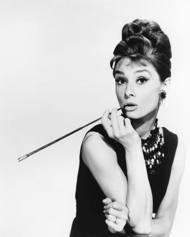 Audrey Hepburn posando com cigarro na boca e virada de lado.