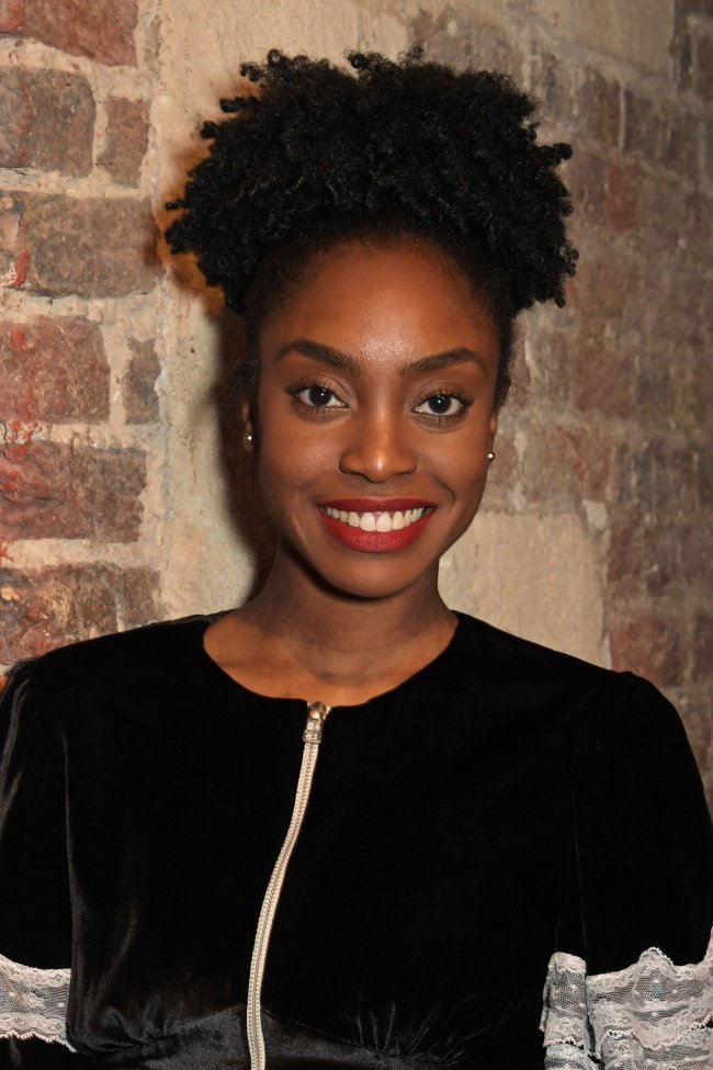 “Cyrano de Bergerac” – Press Night After Party Anita-Joy Uwajeh posando para foto em uma parede de tijolos usando uma roupa preta com detalhes brancos e sorrindo para câmera