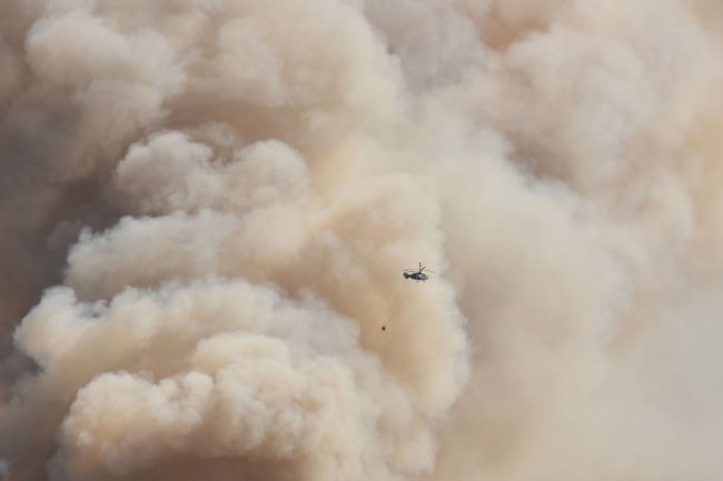 Incêndios na Turquia: causas, como ajudar e o silenciamento do governo Foto de uma imensa nuvem marrom e de um helicóptero pequenininho sobrevoando na frente dela