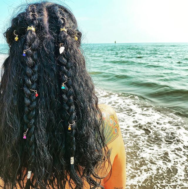 Jovem de costas posando com tranças com piercings por toda extensão.