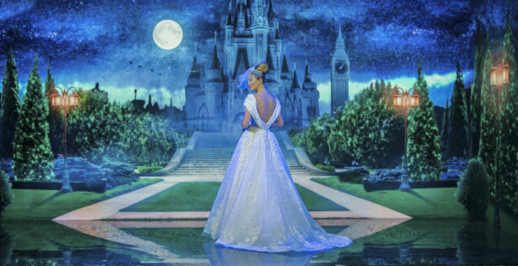 Marthina Brandt com vestido inspirado na Cinderela. Ela está de costas para um fundo que imita o castelo da Disney.