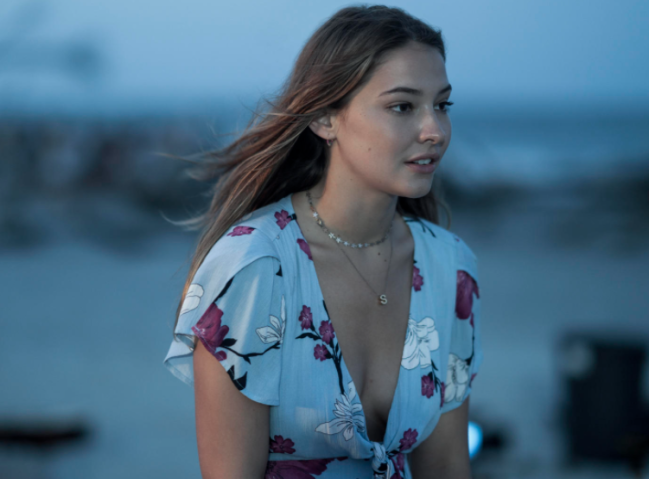 estampa floral outerbanks Sarah olhando para alguma coisa com expressão preocupada, ela está com um vestido com estampa floral.