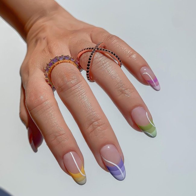 Foto com close nas unhas com esmaltes coloridos em diversas cores.