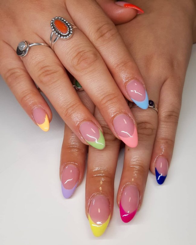 Foto com close nas unhas com esmaltes coloridos em diversas cores.