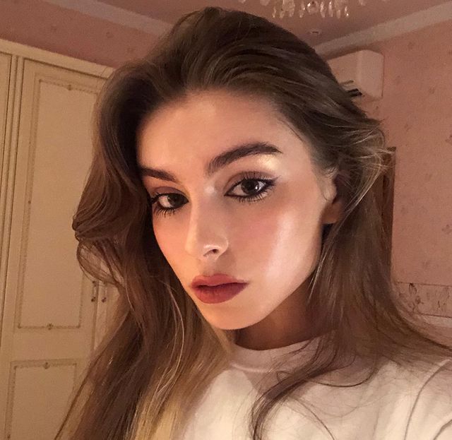 lapis-de-olho-preto-maquiagem Selfie de uma mulher. Ela usa uma blusa branca, cabelo solto, maquiagem com pele natural, batom rosa queimado e olho com lápis de olho preto na linha d'água. Ela olha para a câmera e não sorri.
