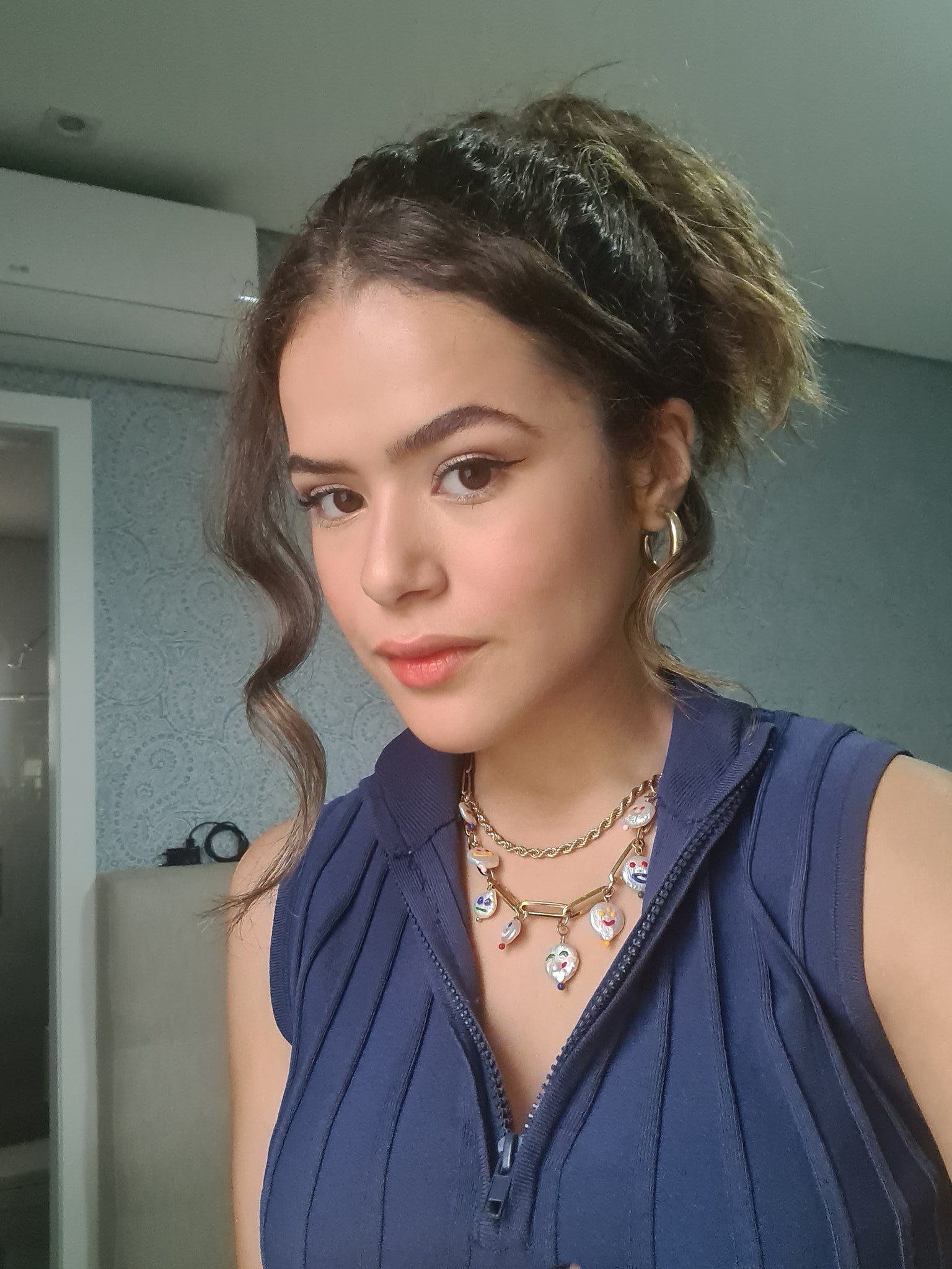 maisa-silva-acessorios-brinco-argola Maisa com o cabelo preso, usando brincos de argola, colares e uma blusa azul, com expressão facial séria