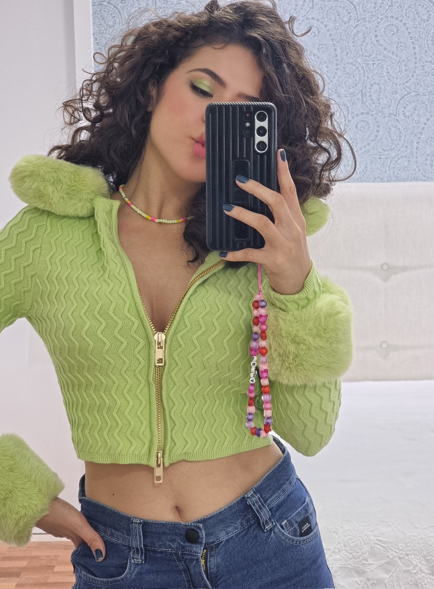 maisa-silva-acessorios-cordinha-celular Maisa Silva usando cardigan verde cropped e calça jeans com celular na frente do rosto em frente ao espelho