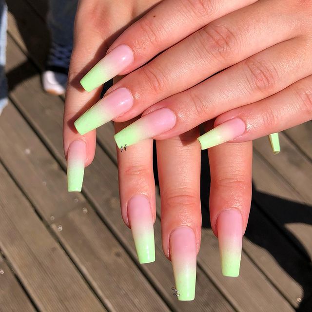 Foto de duas mãos com foco nas unhas decoradas no estilo baby boomer em um tom de verde claro e detalhe de mini argolas nas unhas dos dedos anelares,