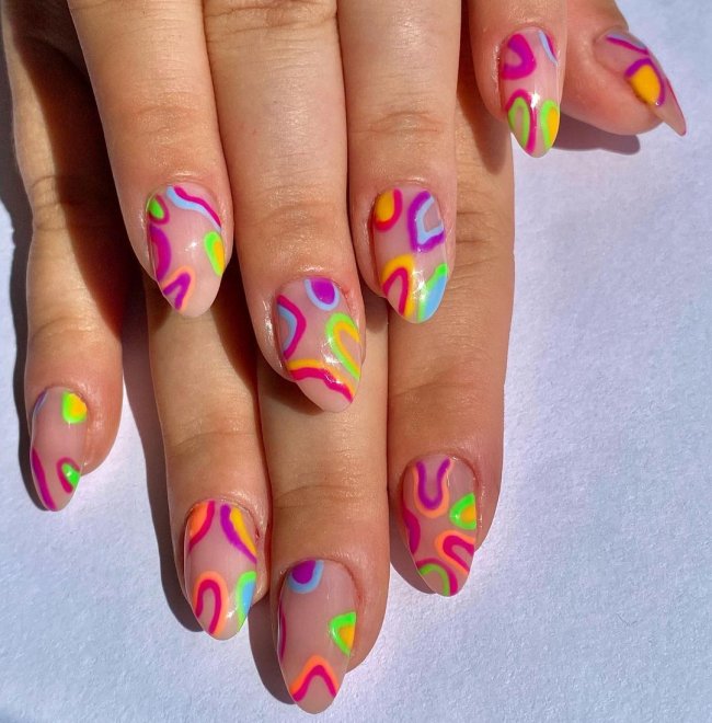 Foto com close nas unhas com esmaltes coloridos em diversas cores.