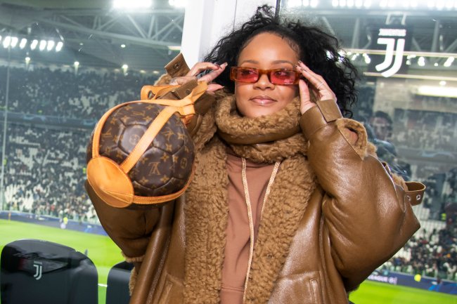 Rihanna ajustando seu óculos vermelho usando bolsa que lembra bola de basquete.