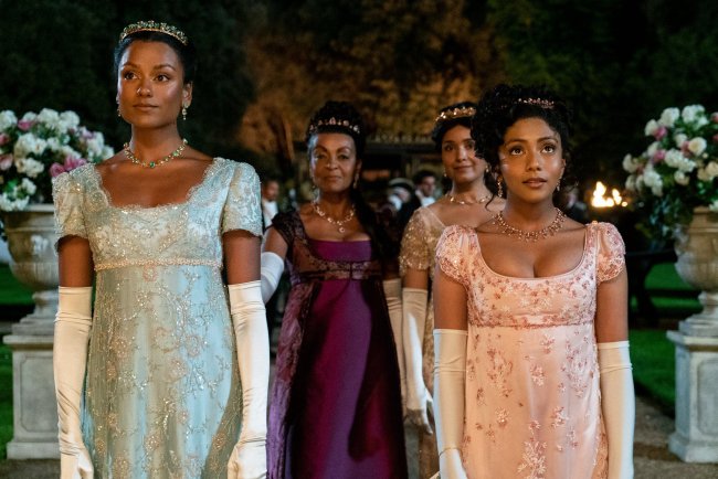 bridgerton segunda temporada Simone Ashley caracterizada como Kate Sharma com vestido azul brilhante de época e luva branca em um baile noturno ao lado de sua família e da rainha em cena da segunda temporada de Bridgerton