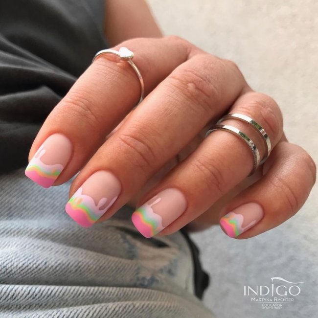 candy-nails Foto de uma mão mostrando as unhas decoradas. As unhas estão pintadas com esmalte rosa claro com detalhes de ondinhas rosa e azul imitando a cobertura de um bolo.