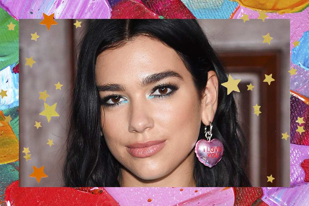 Rosto da Dua Lipa com expressão facial séria, maquiagem preta e azul e brinco de coração rosa em fundo todo colorido com estrelinhas douradas e laranjas