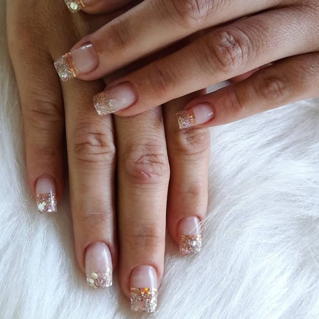 glitter na francesinha Foto de uma mão segurando um esmalte e exibindo as unhas com glitter nas pontas.