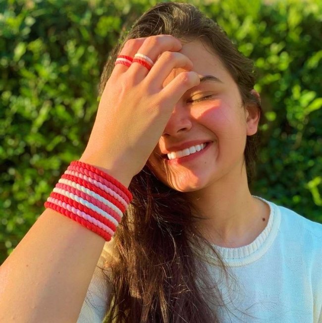 pulseiras coloridas Jovem com uma das mãos no rosto. Ela usa pulseiras e anel nas cores rosa e vermelho.