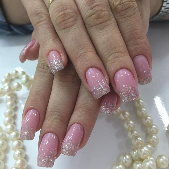 unha rosa com francesinha de glitter Foto de uma mão segurando um esmalte e exibindo as unhas com glitter nas pontas.
