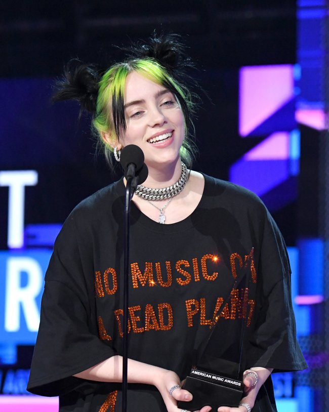 Billie Eilish Billie Eilish segurando prêmio com camisa preta e expressão feliz.