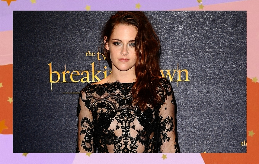 Kristen Stewart usando macacão de renda preto. Seu cabelo está jogado para o lado e ela está com expressão neutra olhando para a câmera