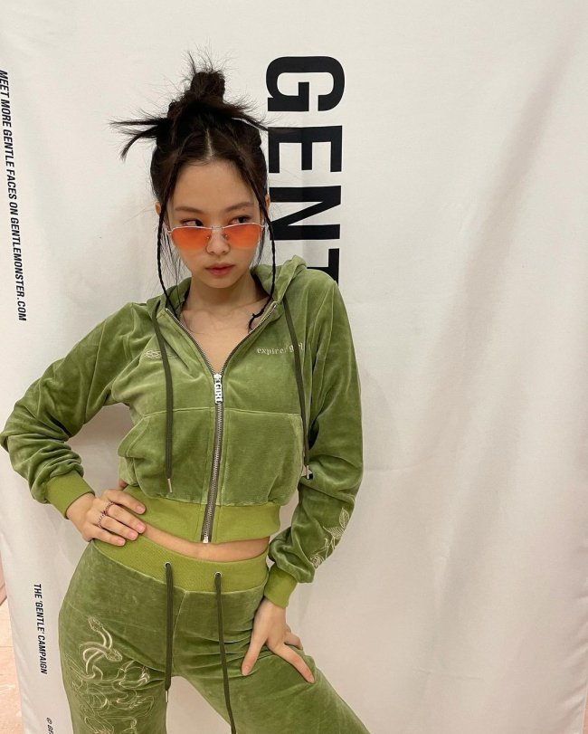 Jennie do BLACKPINK Jennie do grupo BLACKPINK posando com mão na cintura e usando óculos colorido. Ela veste moletom verde aveludado.