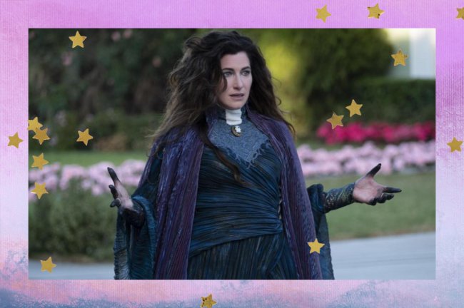 agatha harkness wandavision kathryn hahn Agatha Harkness em cena de WandaVision; ela está com o cabelo solto, usando uma roupa escura com detalhes em verde escuro, preto, branco e roxo, tem expressão chocada e está de braços abertos com as pontas do dedo sujas de preto; a personagem também está olhando para frente em uma área aberta com elementos em verde como árvores e grama; a margem é uma textura em tons de rosa, lilás, azul, branco e roxo com estrelas amarelas como decoração