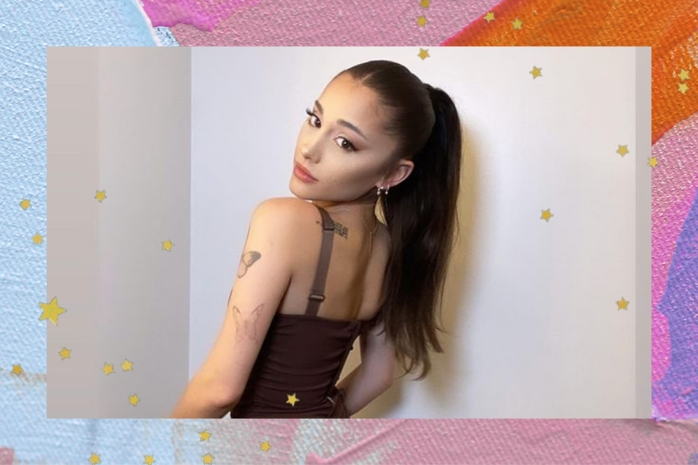 Montagem com o fundo colorido nas cores azul, lilás, roxo e laranja com detalhe de estrelinhas douradas nas bordas com uma foto da Ariana Grande. Ela usa um vestido marrom, cabelo preso em um rabo de cavalo e maquiagem. Ela está de costas, olha para a câmera e não sorri.