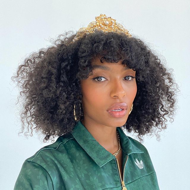 baby-bangs-cabelo-cacheado Selfie de uma mulher. Ela usa um casaco verde, maquiagem natural e cabelo cacheado solto com franja curta. Ela olha para a câmera e não sorri.