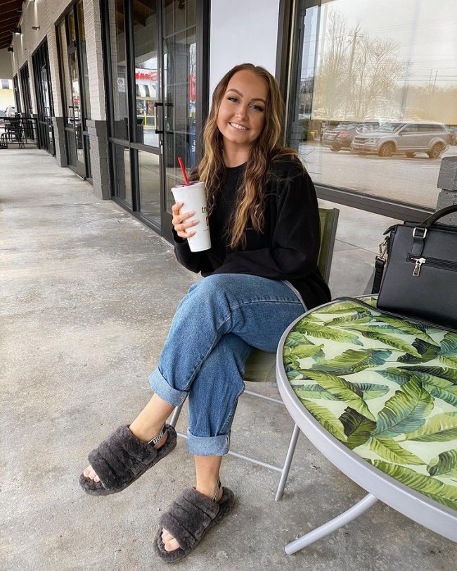 Jovem sorridente posando sentada com calça jeans e camisa preta.