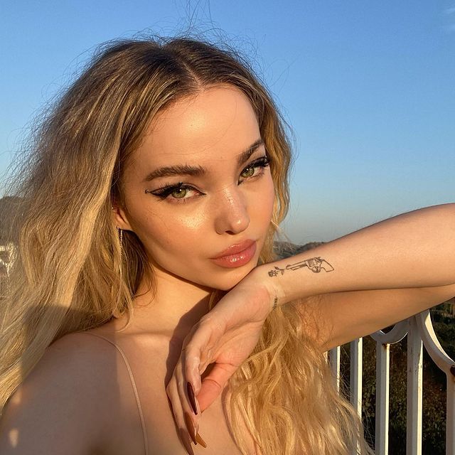 delineado-dove-cameron Selfie da Dove Cameron. Ela usa uma blusa de alcinha, cabelo solto e maquiagem com delineado gráfico preto. Ela está com o queixo apoiado em sua mão esquerda, olha para a câmera e não sorri.