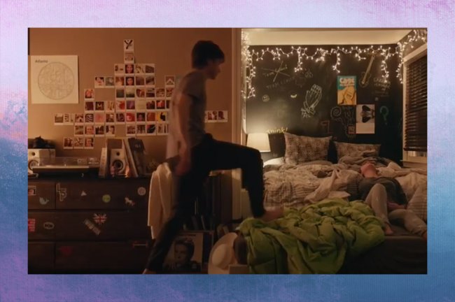 love simon Quarto de Simon, de Com Amor, Simon; ele está subindo na cama com um pé apoiado no colchão e em uma mata verde limão enquanto Abby (Katherine Langford) está deitada; as paredes em volta da cama são de lousa verde escura e na parede ao lado é possível ver um mural de fotos instantâneas e quadros distríbuidos pelo ambiente; a iluminação vem de um abajur em útimo plano e luzes pisca pisca no teto; a margem é uma textura de degradê de rosa, branco, azul. lilás e roxo