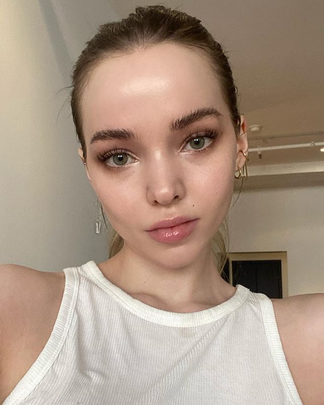 maquiagem-natural-dove-cameron Selfie da Dove Cameron. Ela usa uma blusa branca, cabelo preso e maquiagem com efeito natural. Ela olha para a câmera e não sorri.
