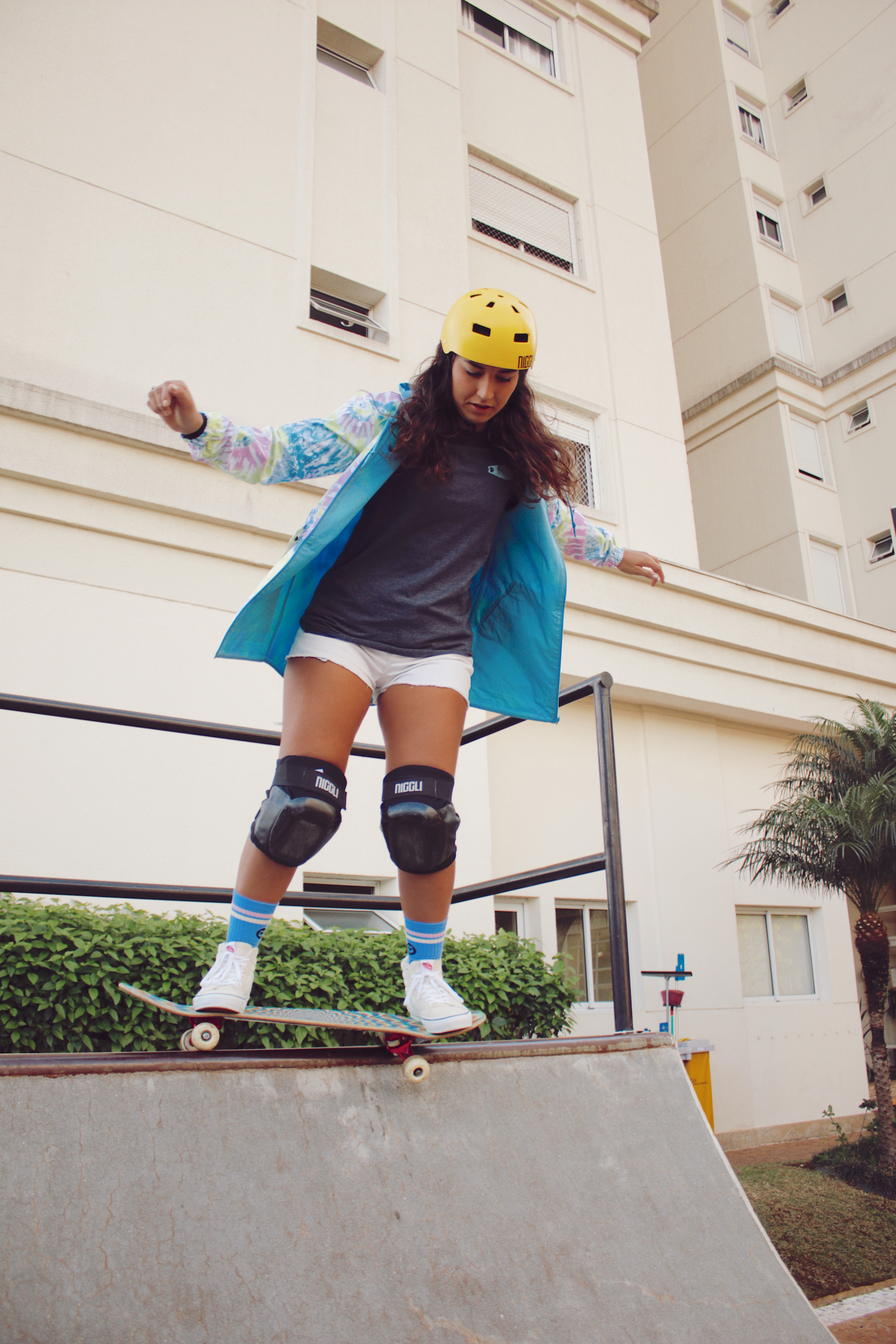 thais-gazarra-34 Thais Gazarra andando de skate em uma mini rampa com jaqueta azul, camiseta cinza, short e capacete e joelheira