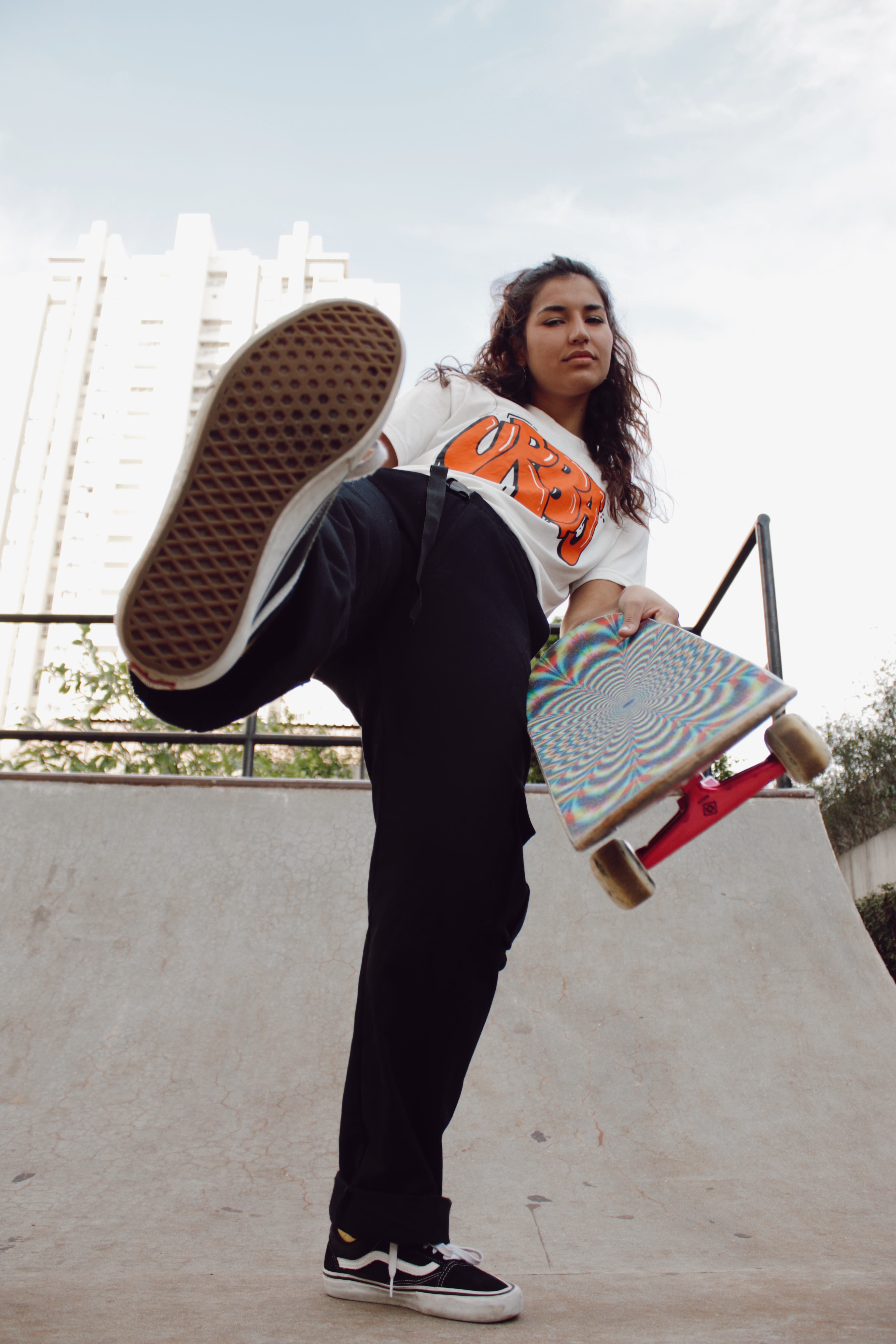 Thais Gazarra usando camiseta branca, calça cargo preta e segurando skate com uma mão